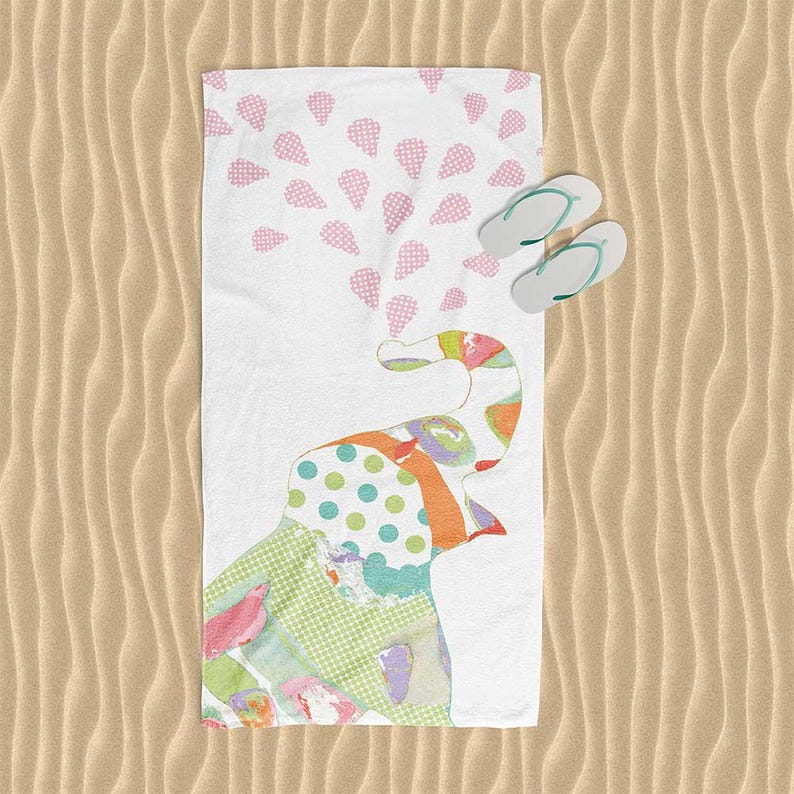A colorful beach towel with a pattern of polka dots and a playful elephant design, along with a pair of flip-flops, is placed on a sandy beach.