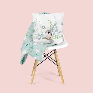 May include: A white chair with a light blue throw blanket and a white pillow with a watercolor illustration of a bird on a branch with green leaves.