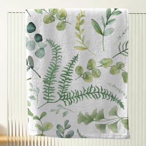 a white towel with a pattern of green leaves and ferns printed on it.