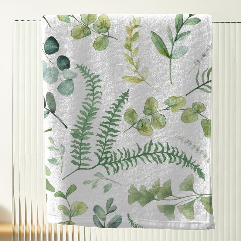 a white towel with a pattern of green leaves and ferns printed on it.