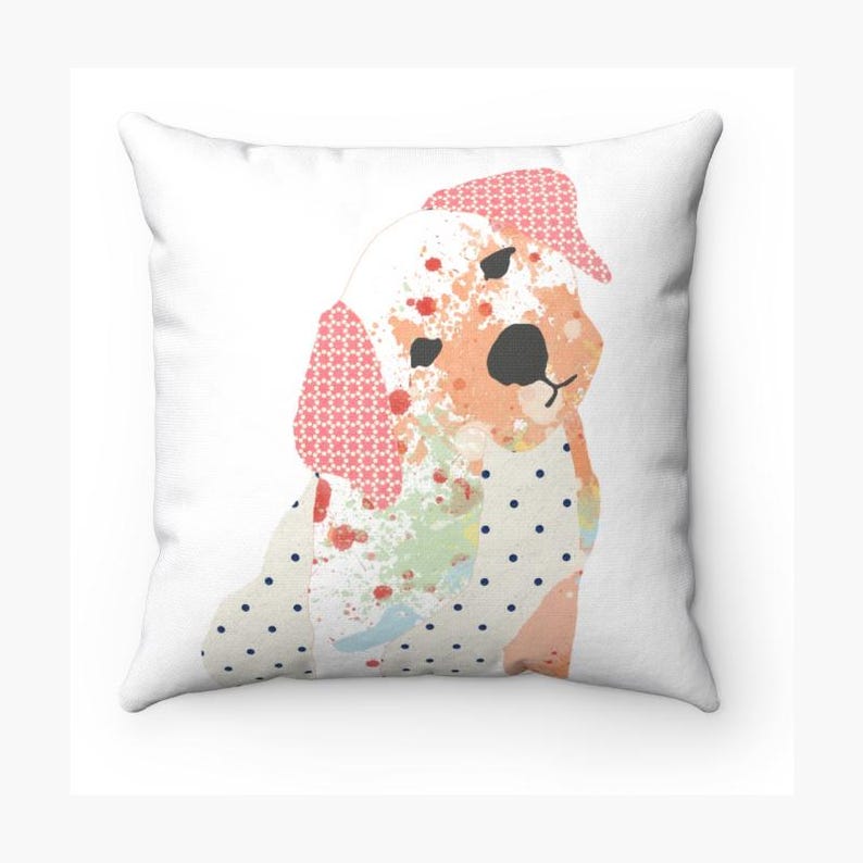May include: A white throw pillow with a colorful patchwork design of a dog. The dog is sitting and has a pink, white, and blue polka dot pattern on its body. The dog's face is a light orange color with a black nose and brown eyes.