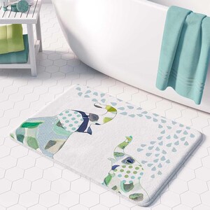 a bathroom with a white bathtub, a colorful elephant-themed bath mat, and a green towel hanging on the side of the bathtub.