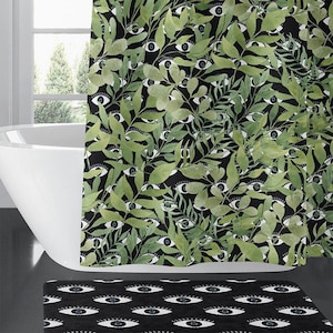 May include: A shower curtain and a matching bath mat featuring a black background with a repeating pattern of white and blue eyes, layered with a dense, overlapping print of green botanical leaves and foliage in various shades of green.