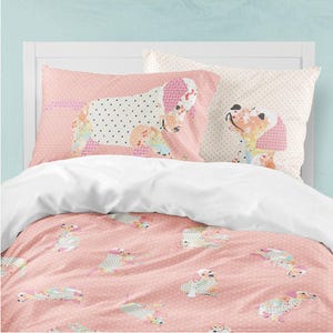 May include: A bedding set featuring a pink duvet cover and two pillowcases decorated with a repeating pattern of stylized dogs. The dogs are rendered in various colorful floral and polka dot patches against a soft pink background with white dots.