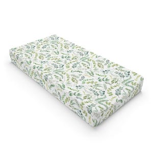May include: A rectangular crib sheet featuring a white background with a repeating pattern of various green botanical leaves, including ferns and eucalyptus sprigs, rendered in a watercolor style across the entire surface of the fabric.