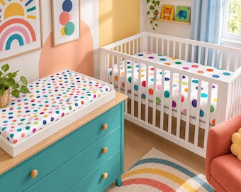 May include: A white wooden crib and a matching changing table topper, both featuring a white fabric cover with a colorful polka dot pattern. The room includes a teal dresser, a rainbow-patterned rug, and wall art depicting a sun and circles.
