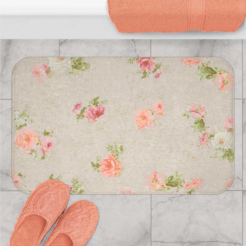 a bathroom scene with a floral patterned bath mat, a pair of pink slippers, and a towel.