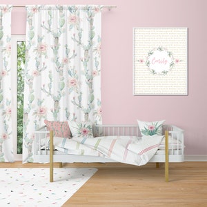 May include: A nursery scene with a white crib, curtains, and a rug. The curtains and pillows feature a cactus and floral pattern in soft green and pink hues. A framed print on the wall displays the name "Emily" within a floral wreath.
