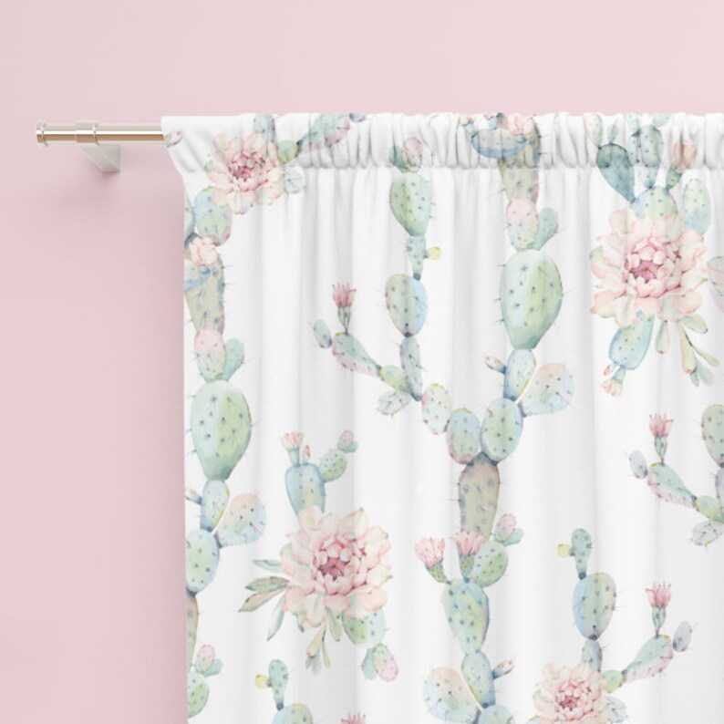 May include: White curtain with a watercolor pattern of cacti and pink flowers. The curtain is hanging from a silver rod against a pink wall. The cacti are light green and blue, with delicate pink flowers.