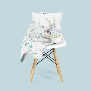 May include: A white chair with a white throw blanket and a pillow with a watercolor design of a bird and green foliage.