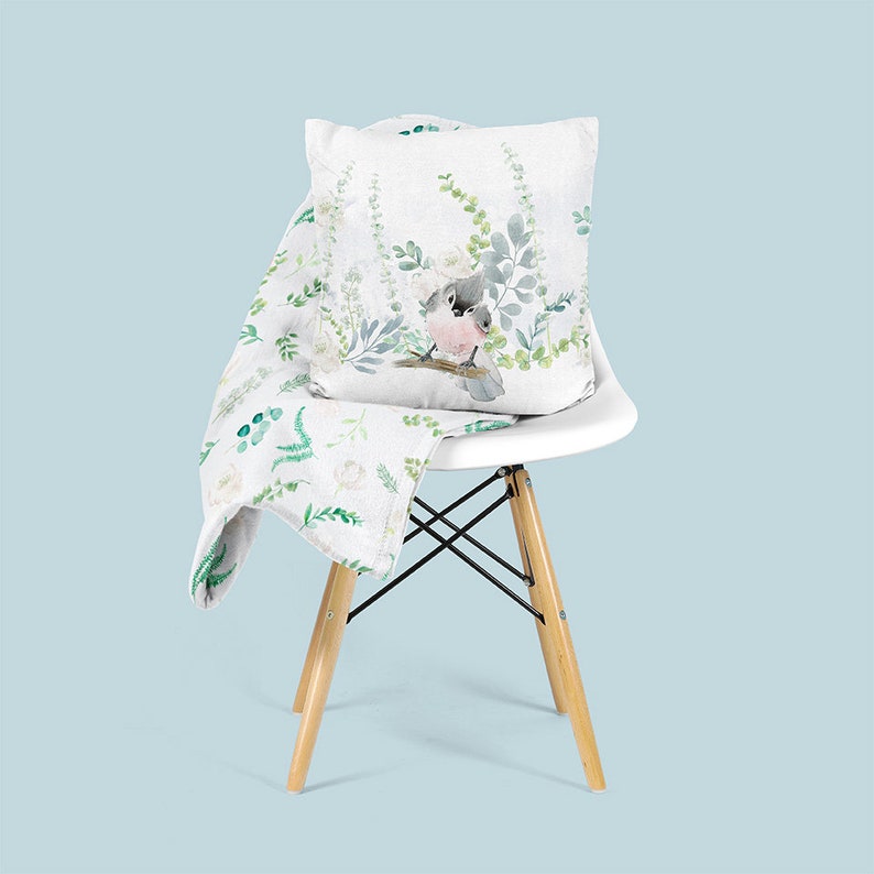 May include: A white chair with a white throw blanket and a pillow with a watercolor design of a bird and green foliage.