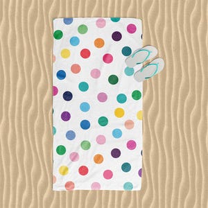 A colorful polka dot towel is spread out on a sandy beach, with a pair of flip-flops placed next to it.