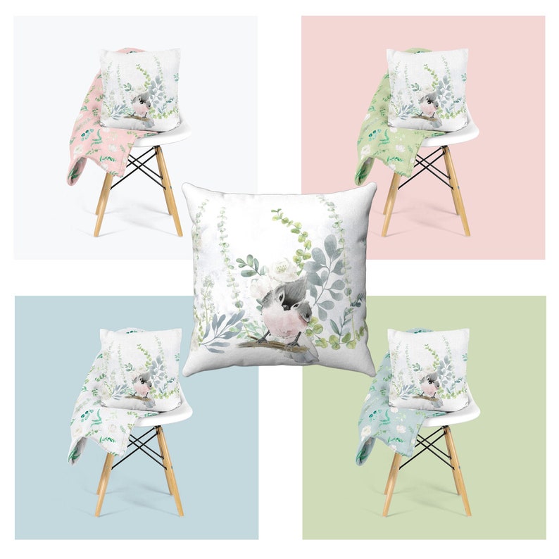 May include: A set of four throw pillows with a watercolor design of two birds perched on a branch with green leaves. The pillows are displayed on white chairs with floral patterned throw blankets.