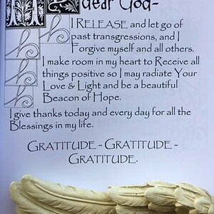 May include: A page with handwritten text, including the phrases "dear God," "I RELEASE," and "GRATITUDE." Decorative initial letters and a sculpted wing are visible. The text is a prayer or affirmation.