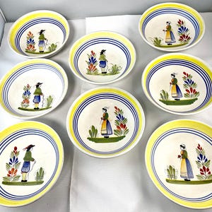 May include: A set of seven round ceramic bowls featuring a hand-painted design of a figure in traditional clothing standing next to a floral arrangement. Each bowl has a yellow rim and concentric blue circular lines on the interior surface.