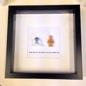 May include: A black framed picture with a white background. The picture features two Lego minifigures, R2-D2 and C-3PO, and the text "These are not the droids you are looking for."