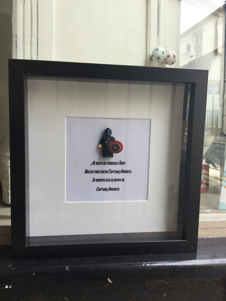 May include: A black framed picture with a white mat and a Lego figurine of Captain America. The quote "ALWAYS BE YOURSELF TOBY, UNLESS YOU CAN BE CAPTAIN AMERICA IN WHICH CASE ALWAYS BE CAPTAIN AMERICA" is printed below the figurine.