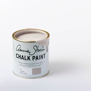 May include: A can of Annie Sloan Chalk Paint in the color Paloma. The can is light blue with gold trim and features the brand name and product information. The paint is a light, neutral color, perfect for furniture and wall projects.