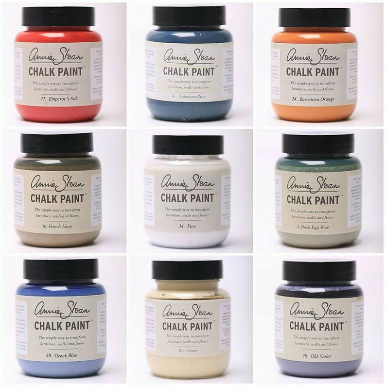 May include: Nine jars of Annie Sloan Chalk Paint in various colors, including red, blue, orange, and green. Each jar has a black lid and a label with the brand name and paint color name. The text on the label reads "The simple way to transform furniture, walls and floors."