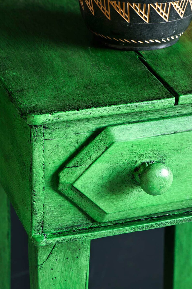 May include: A small green wooden side table with a single drawer and a round knob. The table has a distressed finish and is painted a deep green colour.