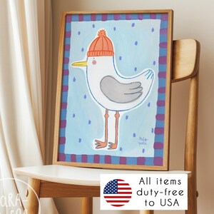 May include: A framed watercolor print of a seagull wearing an orange knit cap. The seagull is white with gray wings and orange legs and feet. The background is light blue with purple dots and a purple and blue plaid border. The print is in a wooden frame.
