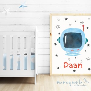 Pu&ograve; includere: Una stampa ad acquerello di un casco da astronauta con stelle e il nome "Daan" in lettere rosse. La stampa &egrave; incorniciata in una cornice di legno chiaro e posizionata su uno sfondo di legno bianco.