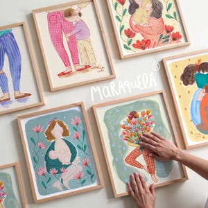 Może przedstawiać: Kolekcja oprawionych wydruk&oacute;w artystycznych z ilustracjami matek i dzieci. Grafiki przedstawiają uściski, karmienie piersią i trzymanie kwiat&oacute;w. Wydruki mają drewniane ramy i są eksponowane na białej ścianie. Widoczny jest podpis artysty.