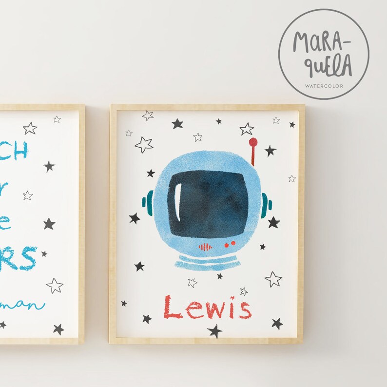 Pu&ograve; includere: Una stampa incorniciata con un'illustrazione di casco da astronauta blu e il nome "Lewis" scritto in rosso. Lo sfondo &egrave; bianco con stelle nere.