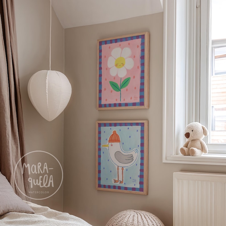 May include: Two framed watercolor prints of a flower and a bird hang on a beige wall. The flower print has a pink background with a white flower and green leaves. The bird print has a blue background with a seagull wearing an orange hat.