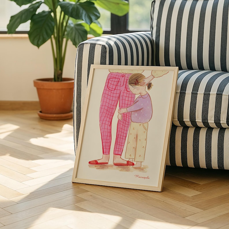 Może przedstawiać: Oprawiony wydruk artystyczny przedstawiający ilustrację dziecka obejmującego nogi osoby. Osoba ma na sobie r&oacute;żowe spodnie w kratę, a dziecko fioletową koszulę i beżowe spodnie. Grafika jest w jasnej drewnianej ramie.