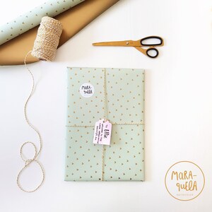 Pu&ograve; includere: Un regalo avvolto in carta verde con cuori dorati e legato con spago. Il regalo &egrave; etichettato con un'etichetta rosa che dice "A Ellie" e un adesivo bianco che dice "Mara-quella".