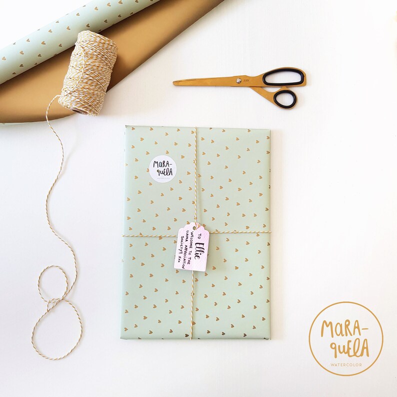 Pu&ograve; includere: Un regalo avvolto in carta verde con cuori dorati e legato con spago. Il regalo &egrave; etichettato con un'etichetta rosa che dice "A Ellie" e un adesivo bianco che dice "Mara-quella".