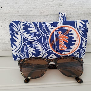 May include: A blue and white Mets-themed glasses case with a matching fabric loop. Tortoiseshell sunglasses rest in front of the case. The case features the Mets logo and team name.