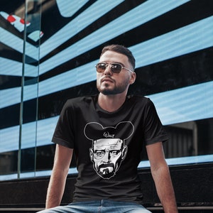 May include: A black t-shirt with a white graphic of Walter White from the TV show Breaking Bad wearing Mickey Mouse ears. The text "Walt" is written on the ears. The person wearing the shirt is looking to the right.