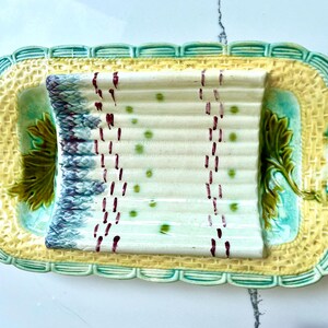 May include: A vintage ceramic serving dish with a raised design of asparagus stalks. The dish is decorated with green, yellow, and white glaze and has two handles.