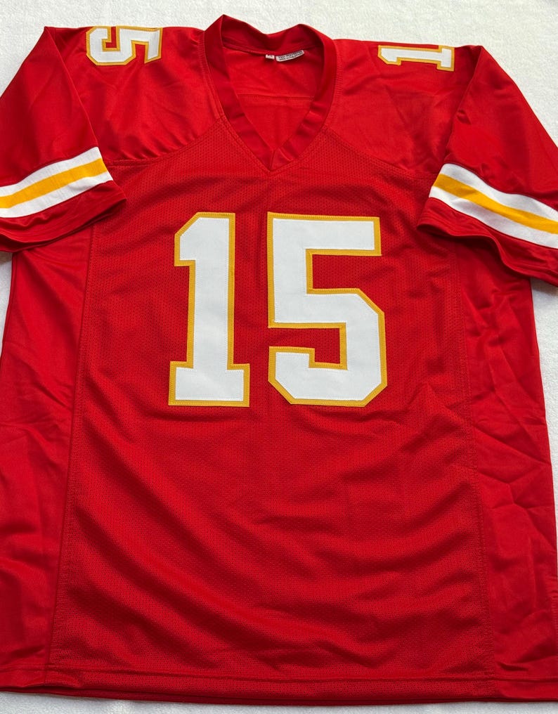 May include: A red football jersey with the number 15 in white with yellow trim on the front. The sleeves have white and yellow stripes. The jersey has a V-neck.