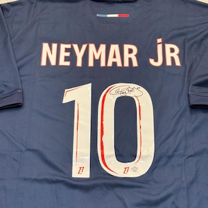 Pode incluir: Camisola de futebol azul marinho com o nome "NEYMAR JR" em letras brancas com contorno vermelho na parte superior das costas. O número "10" é exibido em branco com contorno vermelho. Uma assinatura é visível abaixo.