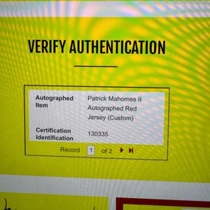 May include: A digital screen displays "VERIFY AUTHENTICATION" with details of an autographed red jersey. The item is identified as a Patrick Mahomes II autographed jersey, with certification ID 130335.