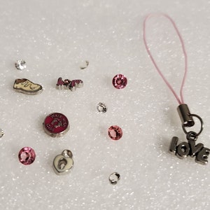 May include: A pink charm bracelet with a variety of charms, including a shoe, a heart, a footprint, and a love charm. The bracelet also includes several pink and clear crystals.