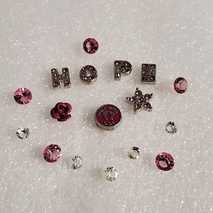 May include: A collection of pink and silver charms, including the word "HOPE", a rose, a star, a footprint charm that says "Walk with God", and several small pink and clear crystals.