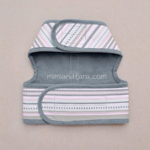 May include: A gray and pink striped dog harness with adjustable straps and a velcro closure. The harness has the website "mimiandetara.com" printed on it.