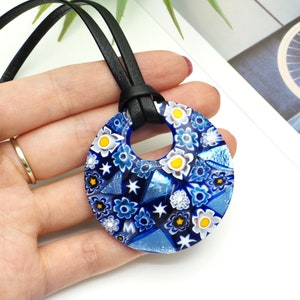 May include: A blue and white glass pendant necklace with a floral pattern. The pendant is round and has a hole in the centre for the cord to go through. The cord is black leather.