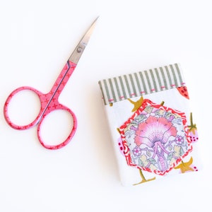 Puede incluir: Un estuche de tijeras de tela rosa con un diseño floral y un par de tijeras pequeñas de color rosa.