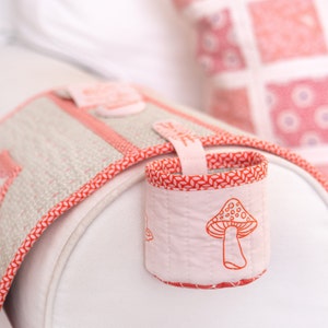 May include: A pink and red fabric armrest with a built-in cup holder. The cup holder has a mushroom design and is perfect for holding a drink.