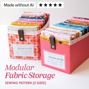 May include: Two rectangular fabric storage bins filled with folded quilting cotton fabric. The left bin features an orange geometric pattern, while the right bin is pink with white dots. Each bin has a brown leather tab and a clear label holder.