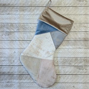 May include: A beige, blue, and white patchwork Christmas stocking with a velvet cuff.