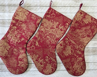 Set of three cranberry red and gold nativity toile Christmas stockings with stable scene, wise men, shepherds, star