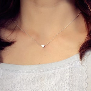 Puede incluir: Un delicado collar de plata con un pequeño colgante triangular.