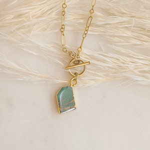 May include: A gold chain necklace with a toggle clasp and a green stone pendant.