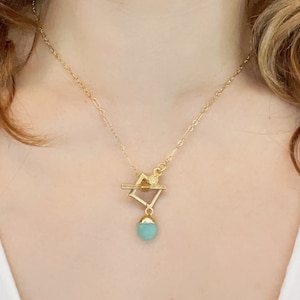 May include: A gold chain necklace with a geometric pendant featuring a square frame and a teardrop-shaped turquoise stone.